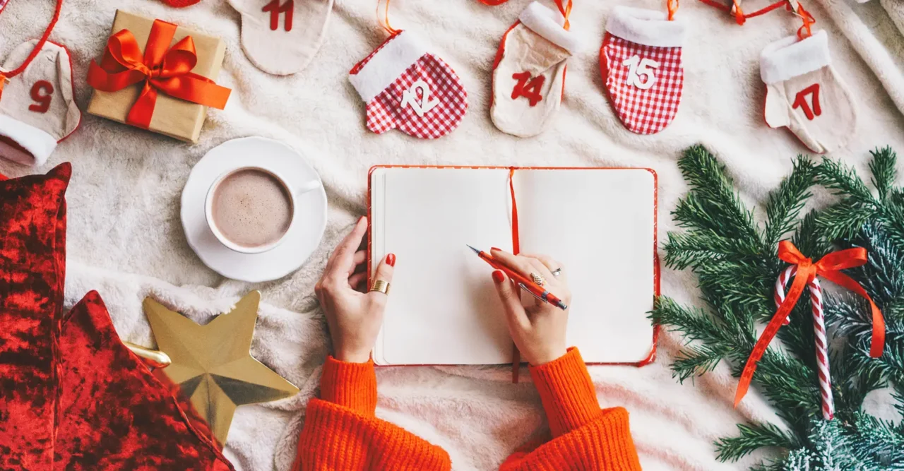 A person wearing red, writing on a holiday-themed and decorated table